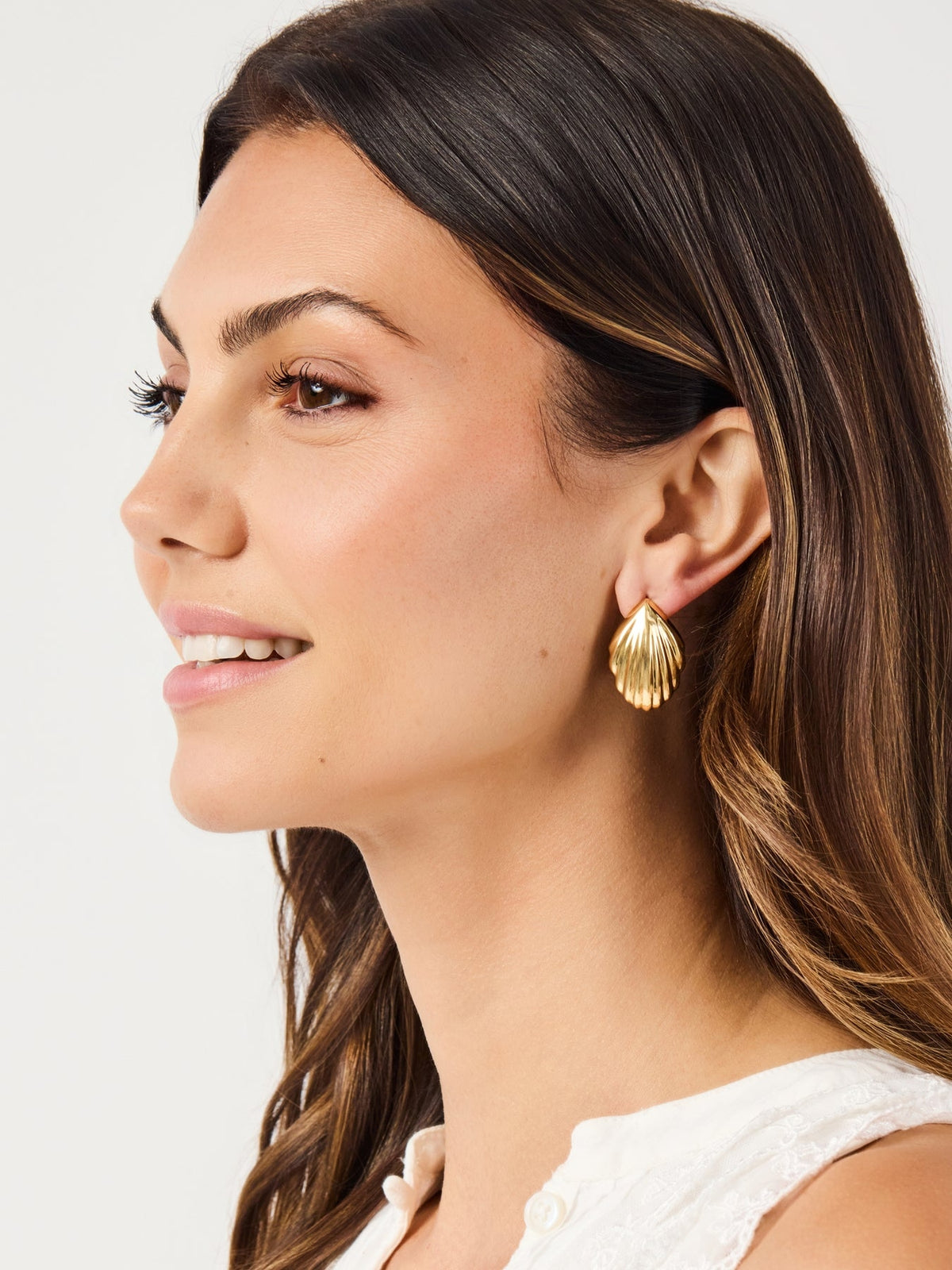 A woman wearing a gold-plated Skyla shell-shaped earring with a ribbed texture.