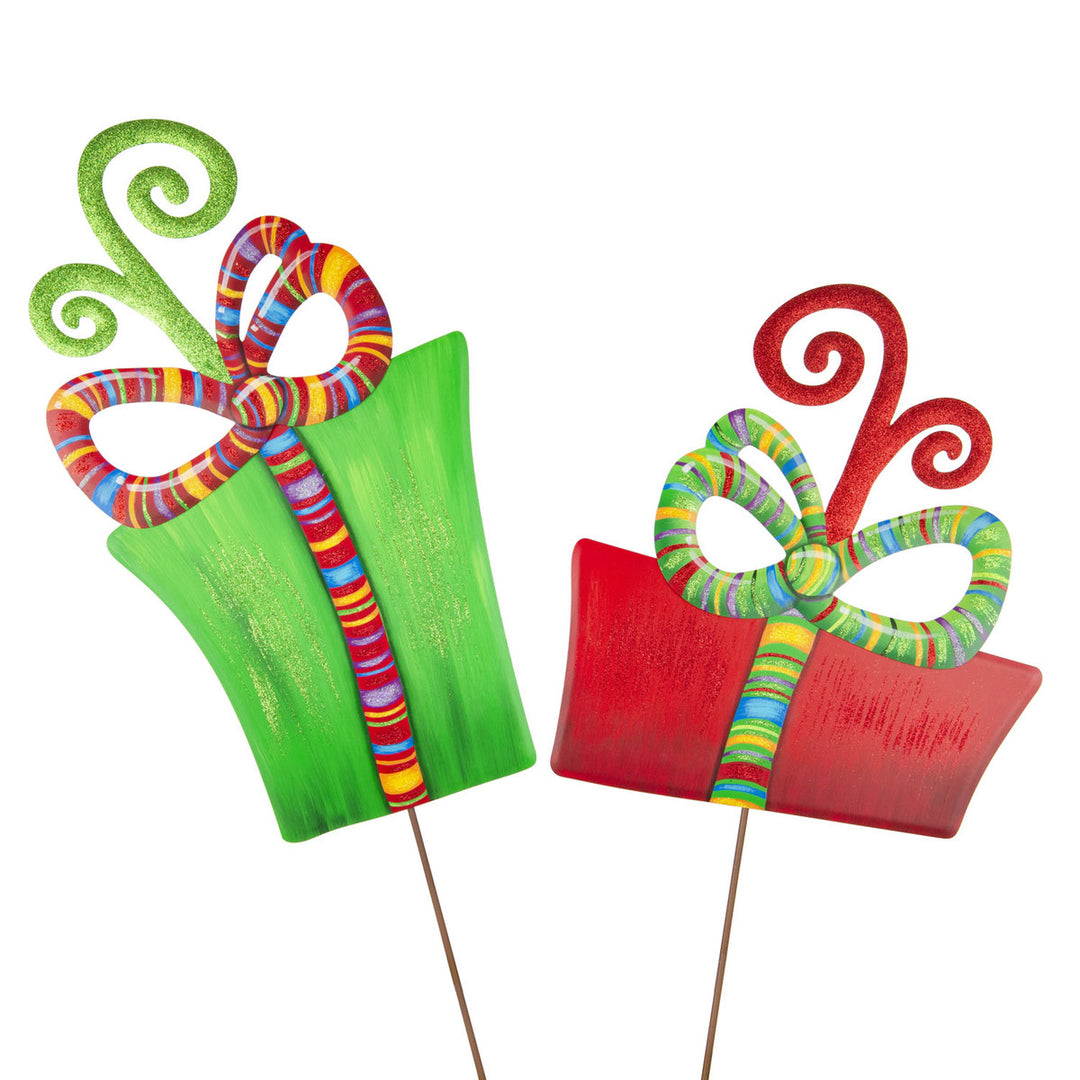 Two colorful metal gift box yard stakes in green and red with striped bows and glitter accents.