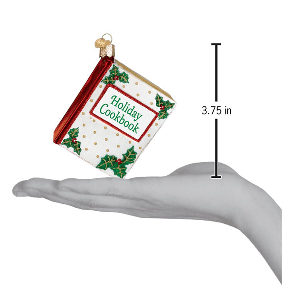 Holiday Cookbook glass ornament with holly details, shown next to a 3.75 inch scale.