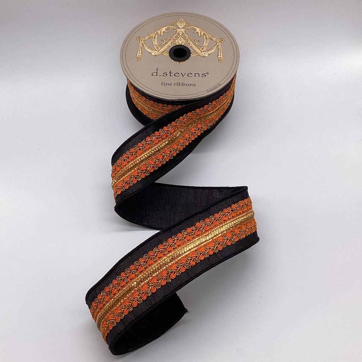 2.5 inch black metallic dupion ribbon with orange and copper embroidered center trim on a spool.