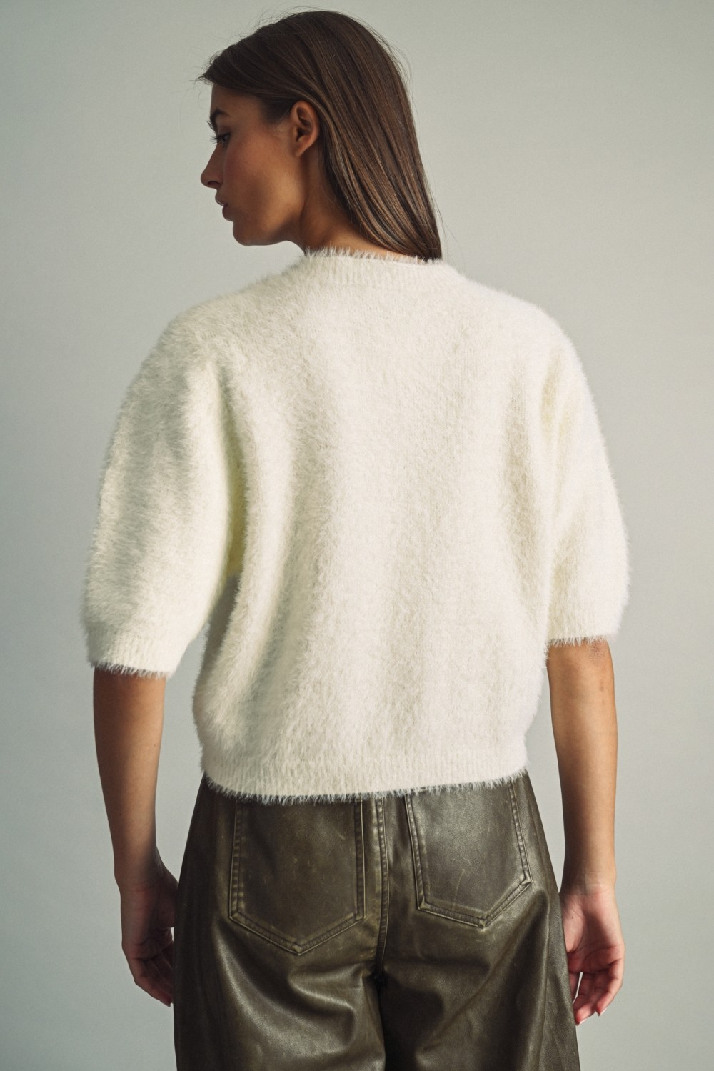Back view of a woman wearing a white fluffy cropped faux-fur sweater with elbow-length sleeves.
