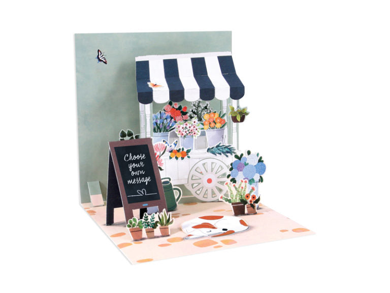 White envelope with gold foil finish containing a square card featuring colorful floral illustrations.