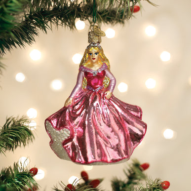 Glass princess ornament in a pink gown hanging on a Christmas tree branch.