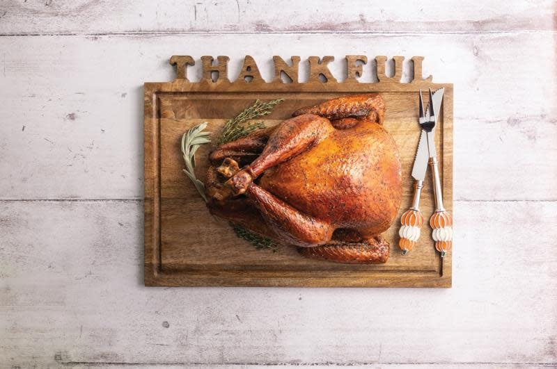 Mango wood carving board with cut-out letters paired with metal utensils featuring enamel pumpkin handles.