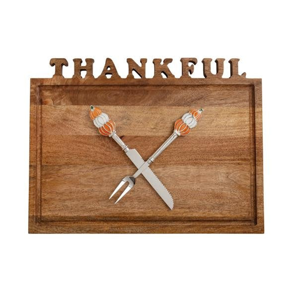 Mango wood carving board with cut-out letters paired with metal utensils featuring enamel pumpkin handles.