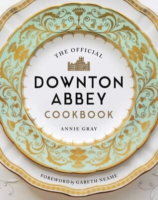 The Official Downton Abbey Cookbook standing upright with a cream cover featuring black serif typography and period illustrations.