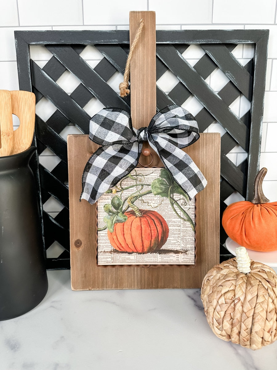 Mini pumpkin print on a wooden board with a black and white buffalo check bow and hanging twine.