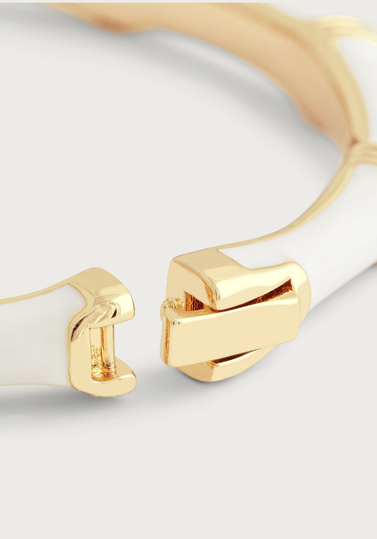 Close-up of a white enameled bamboo-style hinged bangle with a gold-plated clasp.