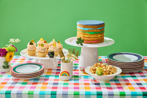St. Patrick's Day table setting with a layered cake, cupcakes, gold coins, and festive decor on a plaid tablecloth.