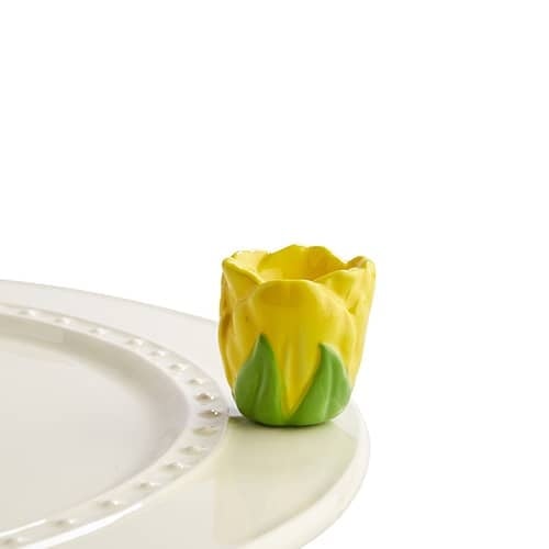 Yellow ceramic tulip-shaped mini decorative accent piece sitting on the edge of a white plate.
