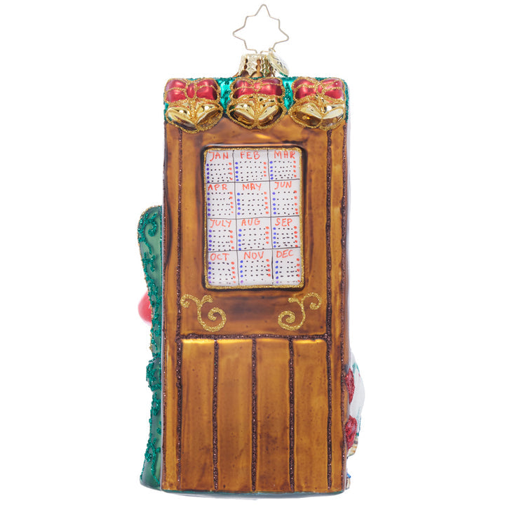 Glass Christmas ornament shaped like a wooden door with a calendar and bells.