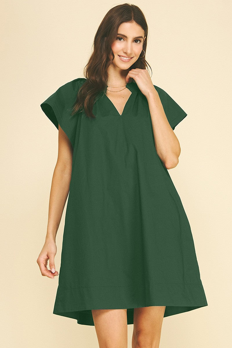 Woman wearing a dark green Amelia Ruffle Detailed Tunic Mini Dress with a V-neckline.