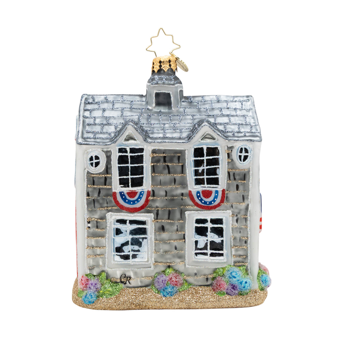 Glass beach house ornament with patriotic bunting, glittery roof, and colorful flower bushes.