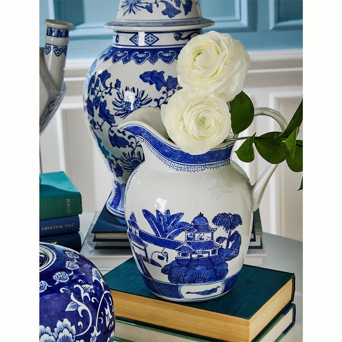 Canton ceramic blue and white pitcher with traditional landscape pattern holding white flowers.
