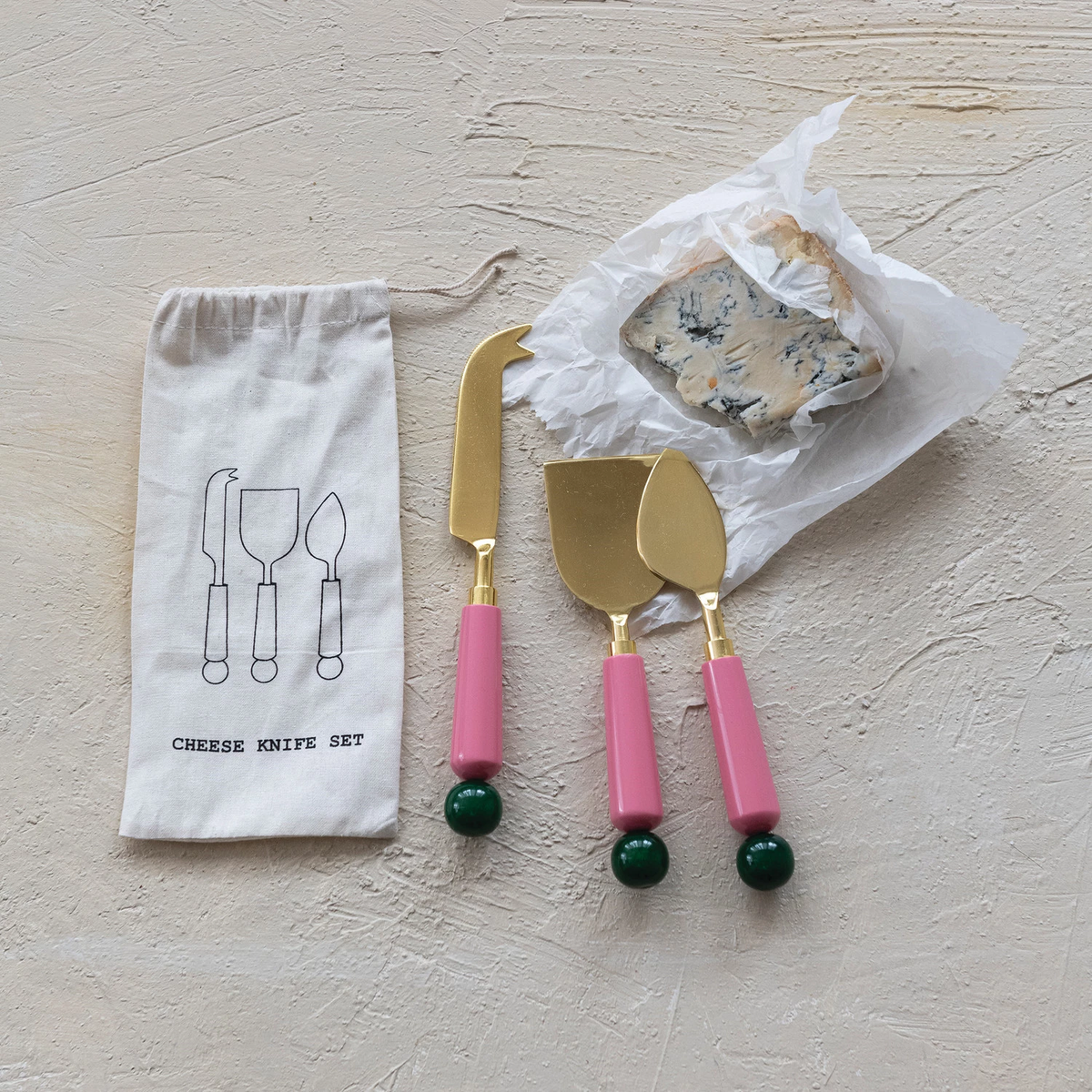 Set of stainless steel cheese knives with dark resin handles in a drawstring bag.