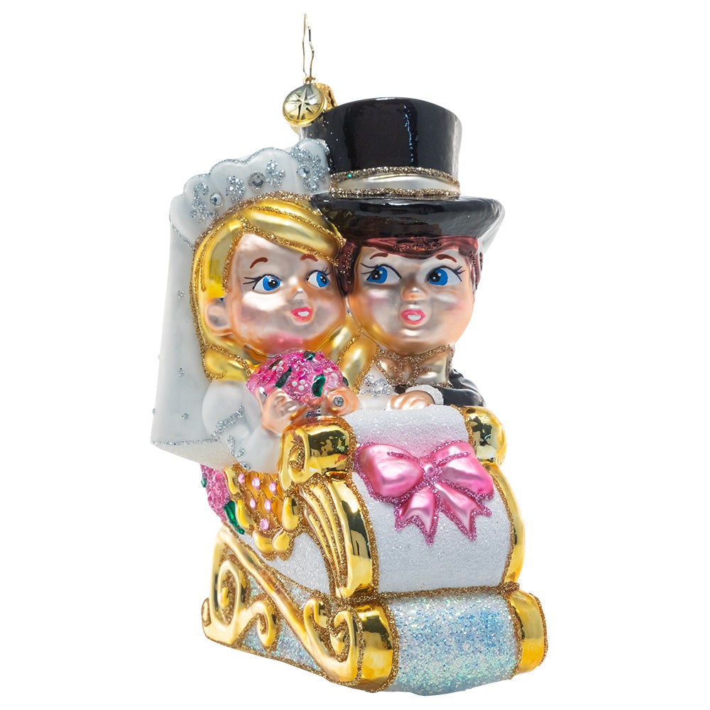 Glass Christmas ornament of a bride and groom in a glittery white and gold sleigh.
