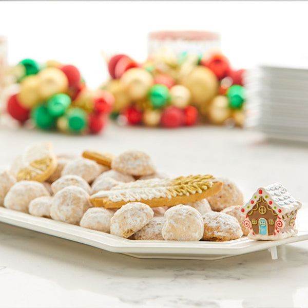 A white platter filled with powdered snowball cookies and a gingerbread house.