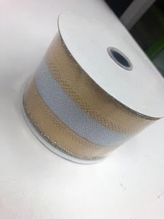 A roll of 2.5-inch wide metallic ribbon featuring alternating beige and silver textured stripes.