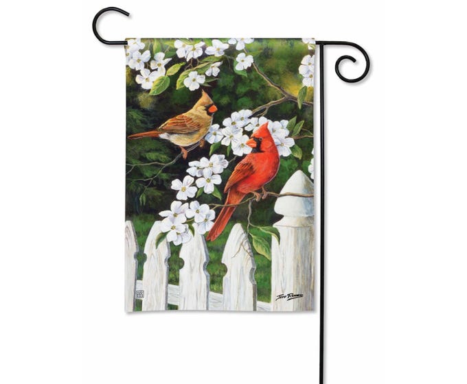 Garden flag featuring two cardinals perched on a white picket fence surrounded by white flowers and green foliage.