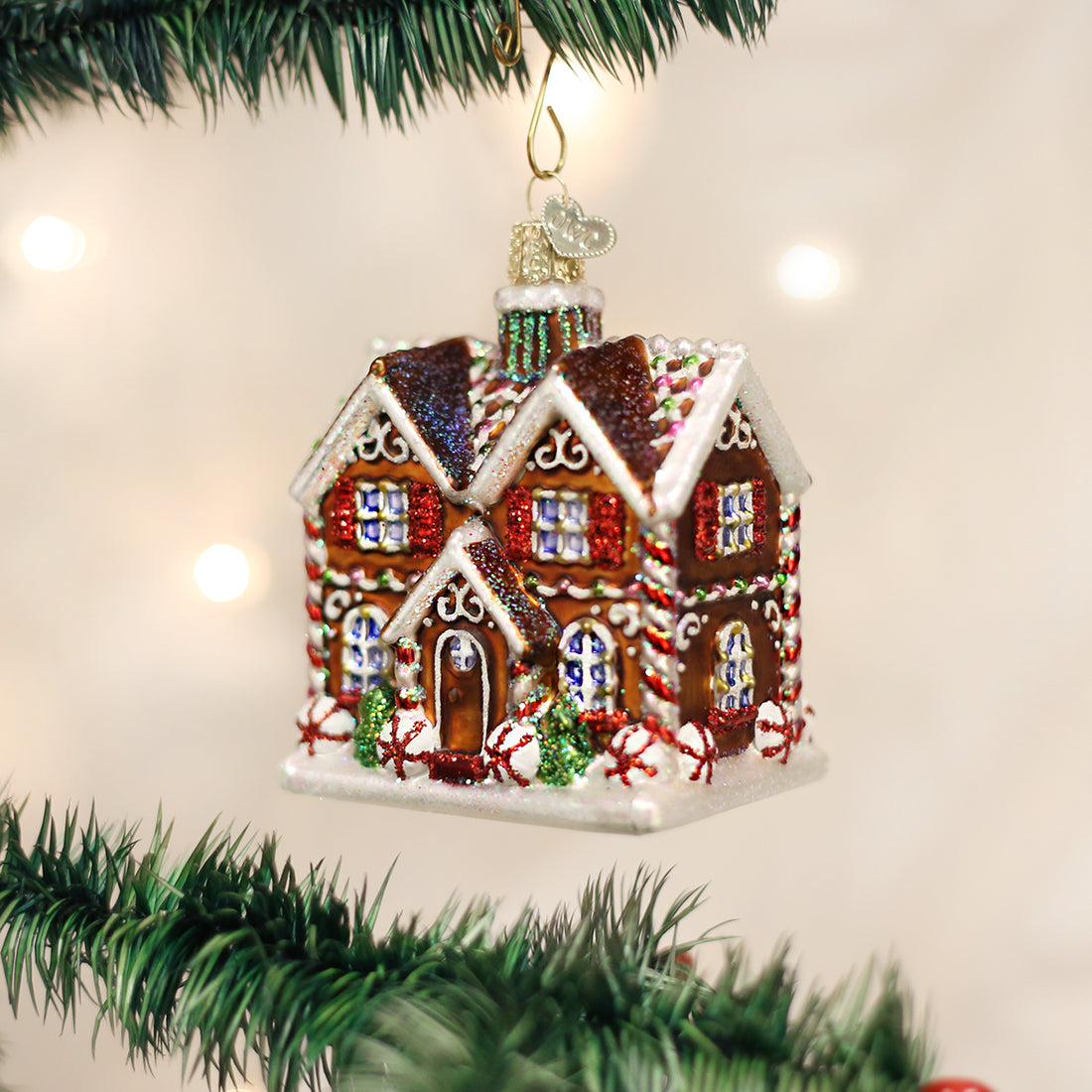 Glittery gingerbread cottage Christmas ornament hanging on a pine tree branch.