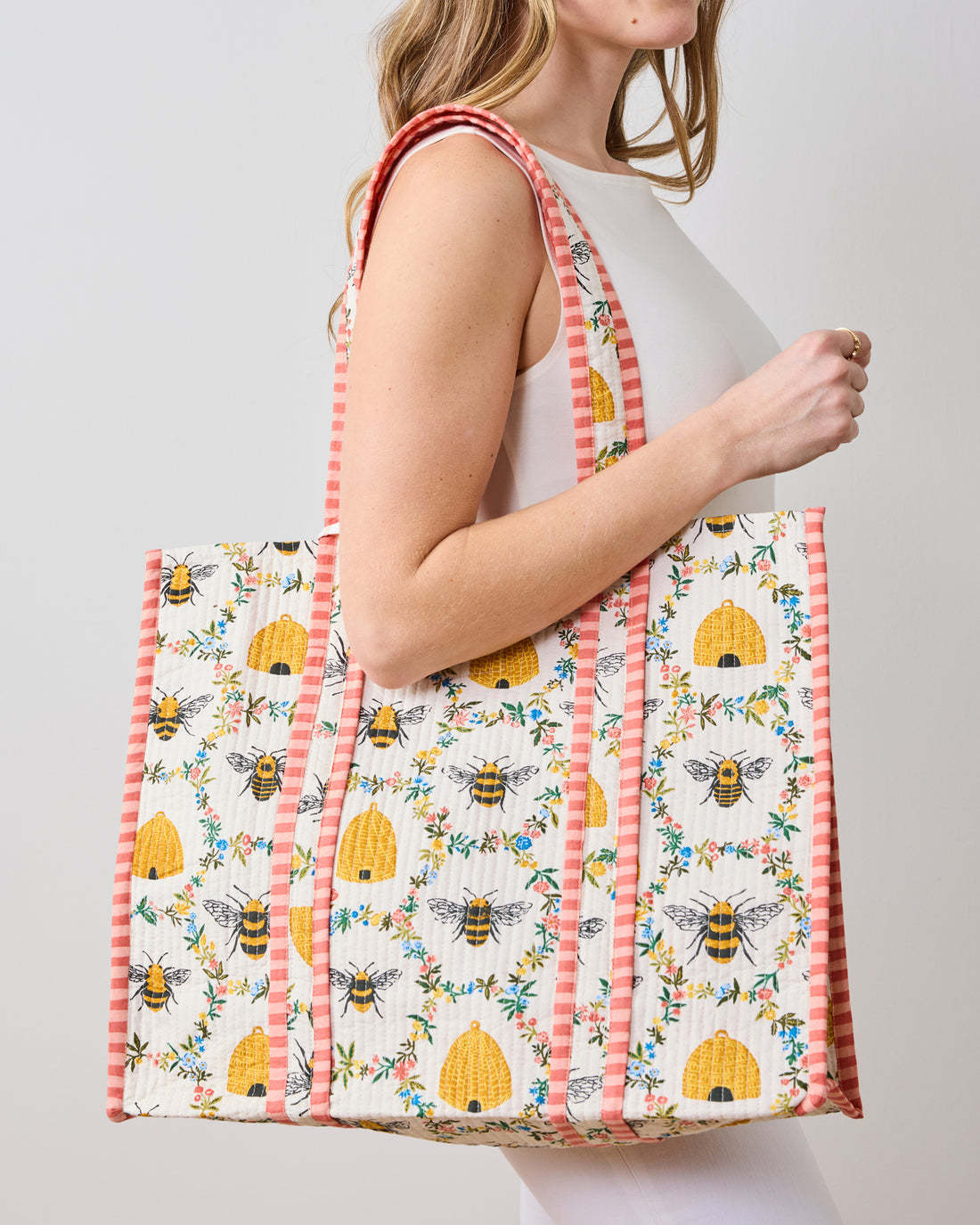 A person carrying the Traveler Tote in Sweet Bee, featuring a quilted bee and beehive pattern.