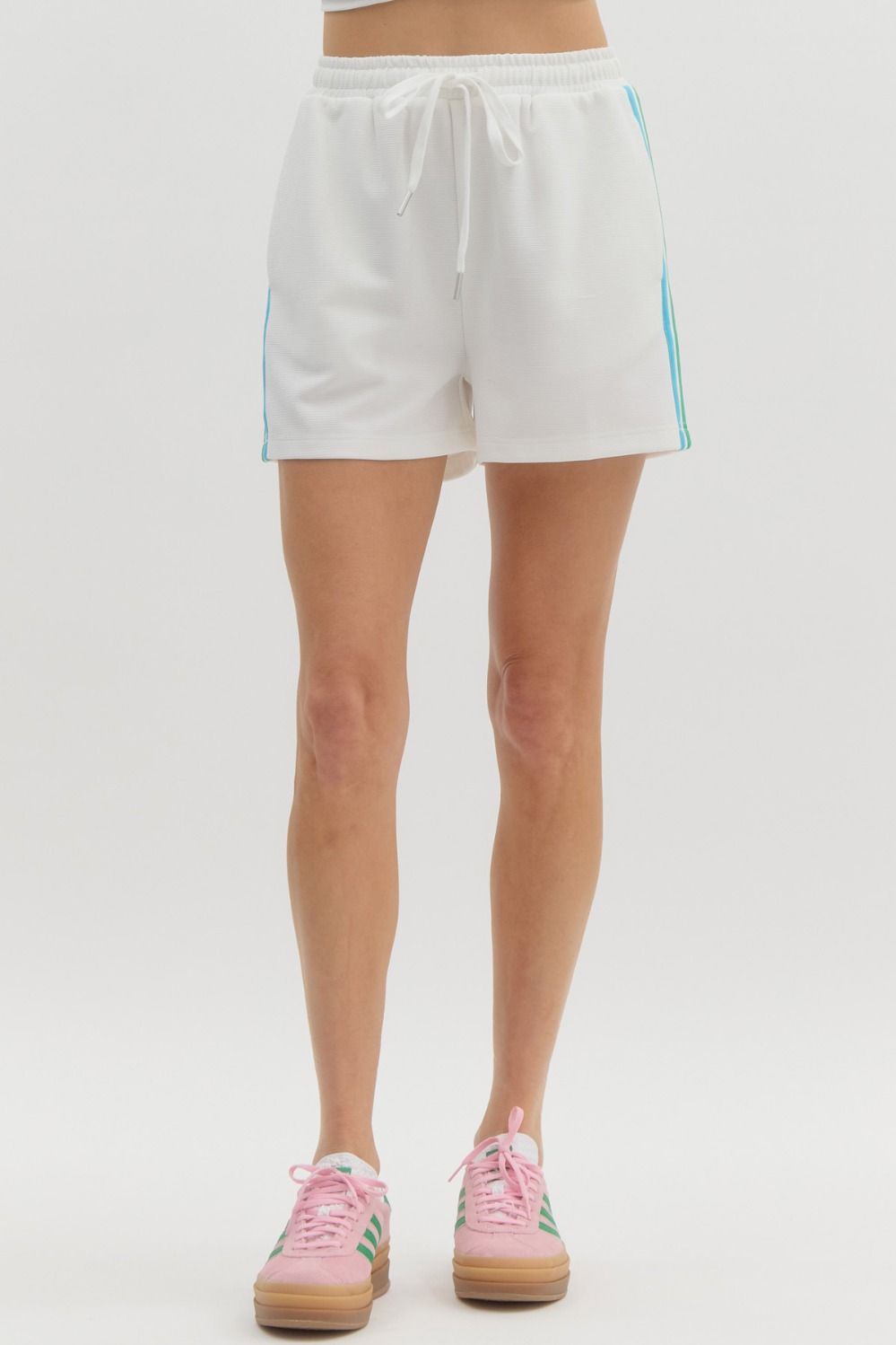 Woman wearing white Jasmine Jersey Knit Shorts with blue side stripes and pink sneakers.
