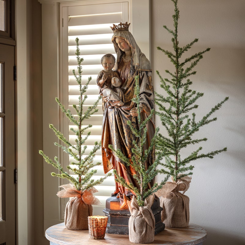 Large Gilded Madonna and Child Statue standing on a table flanked by small burlap-wrapped pine trees