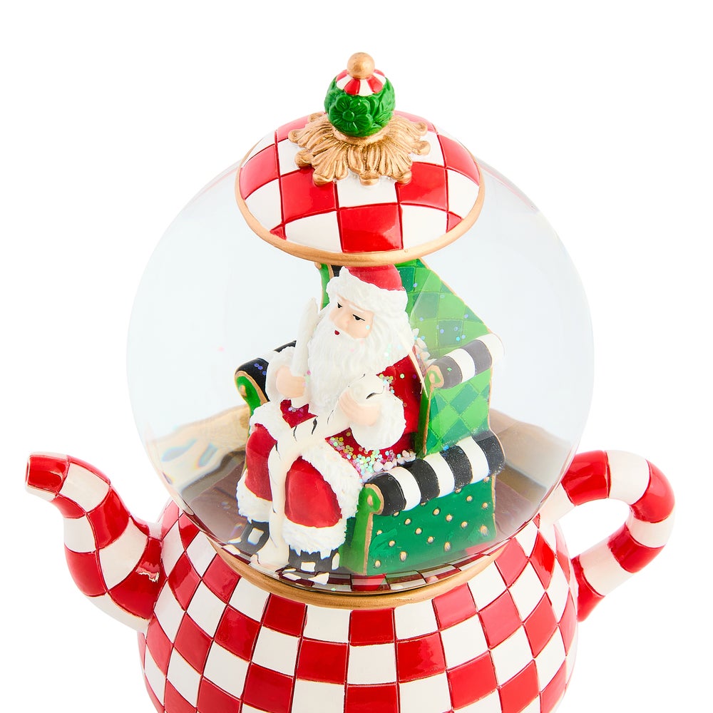 Check It Out Teapot Snow Globe featuring Santa in a green chair inside a red and white checkered pot.