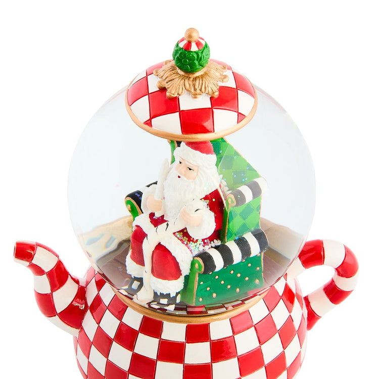 Check It Out Teapot Snow Globe featuring Santa in a green chair inside a red and white checkered pot.