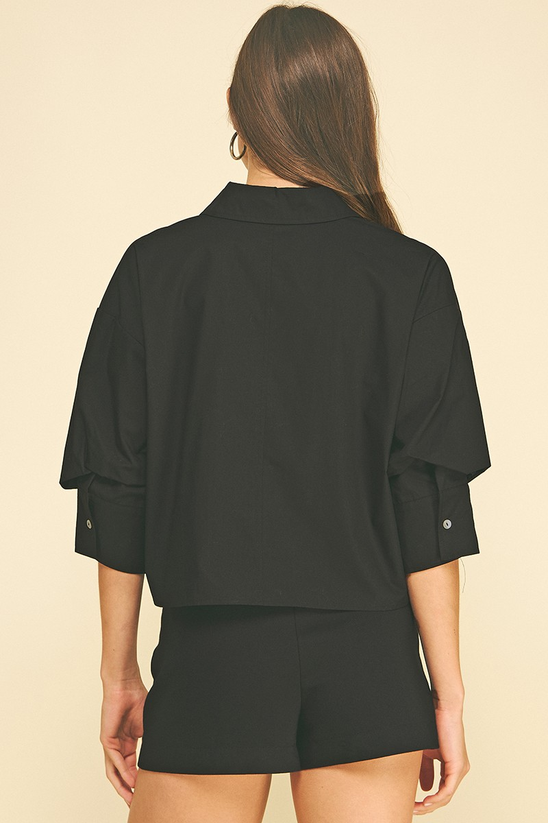 Back view of a woman wearing a black cropped button-down shirt with tuck detailed 3/4 sleeves.