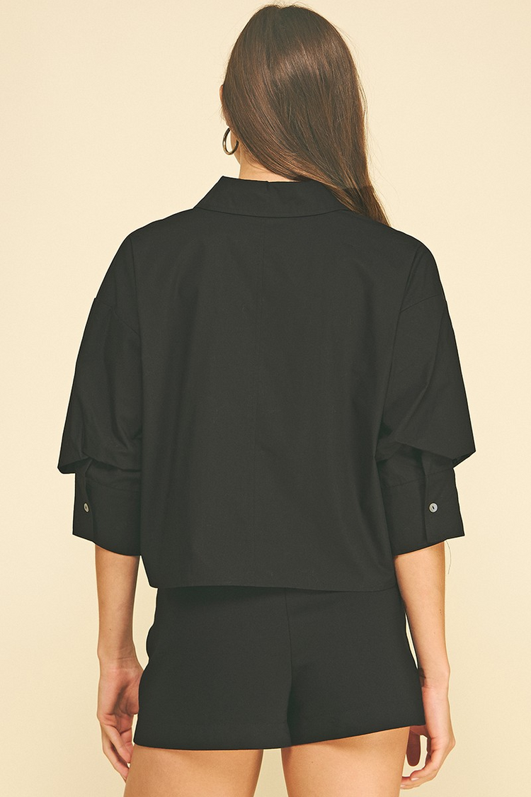 Back view of a woman wearing a black cropped button-down shirt with tuck detailed 3/4 sleeves.
