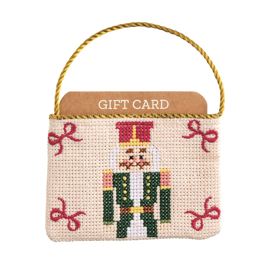 Needlepoint gift card pouch featuring a nutcracker design with a gold cord hanger.