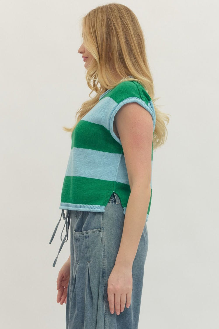 Side view of a woman wearing a green and light blue striped cap sleeve knit top with denim pants.
