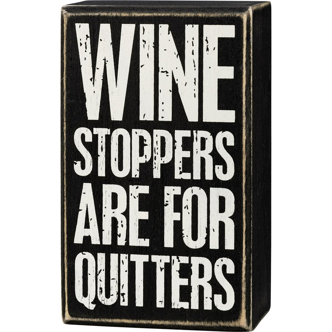 Black wooden box sign with white distressed text reading "WINE STOPPERS ARE FOR QUITTERS".