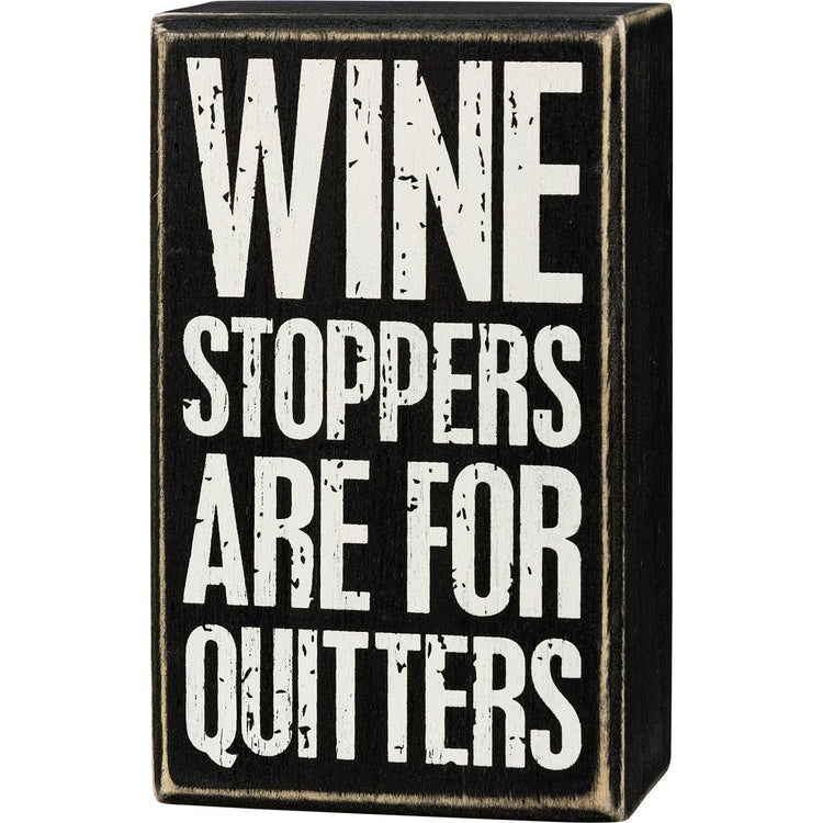 Black wooden box sign with white distressed text reading "WINE STOPPERS ARE FOR QUITTERS".