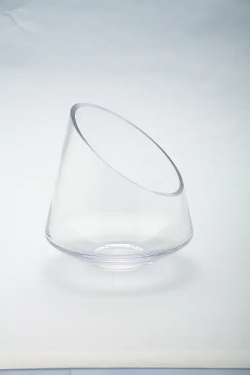Clear round glass bowl with a slanted, angled rim on a white background.