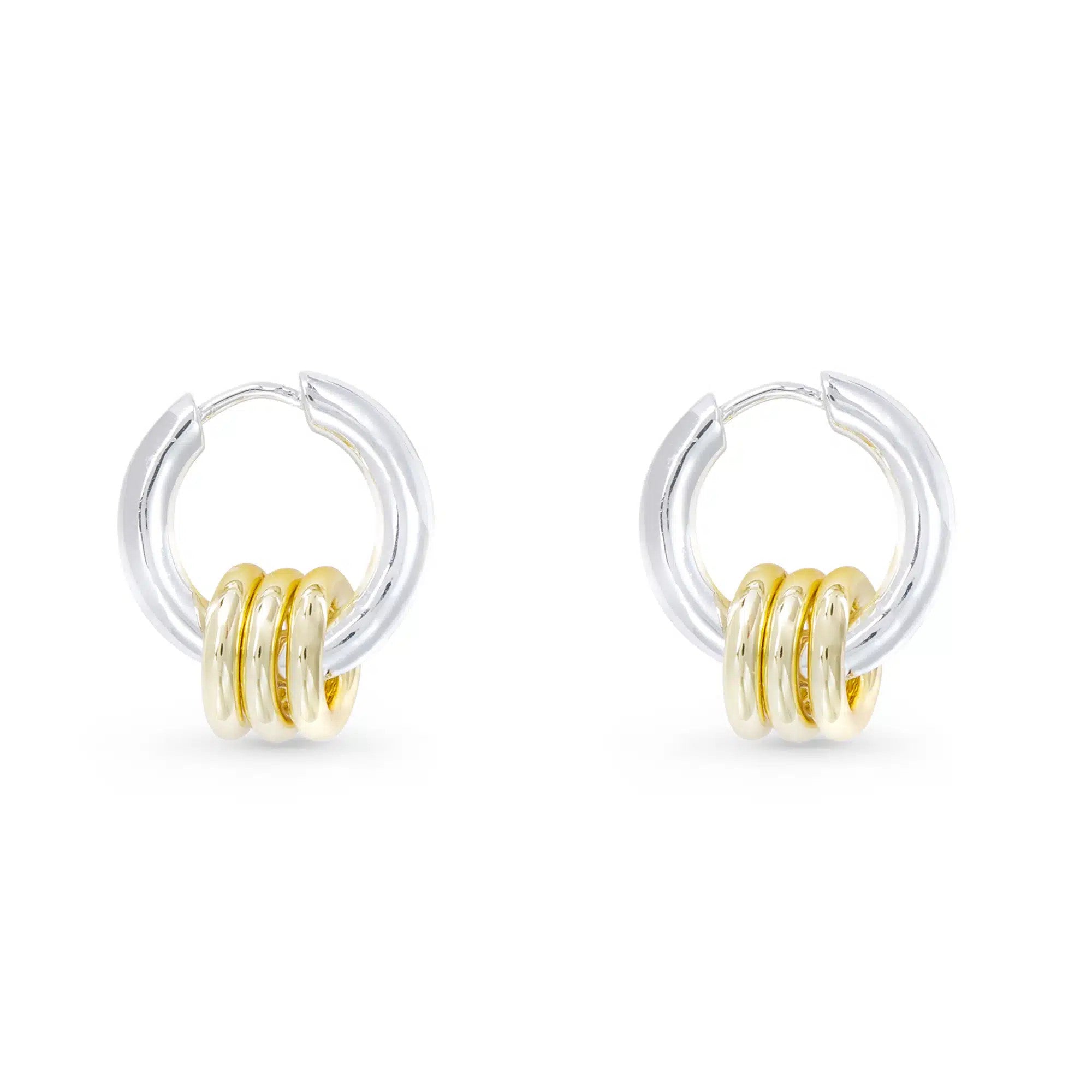 Polished silver huggie hoop earrings featuring three small gold rings on each hoop.