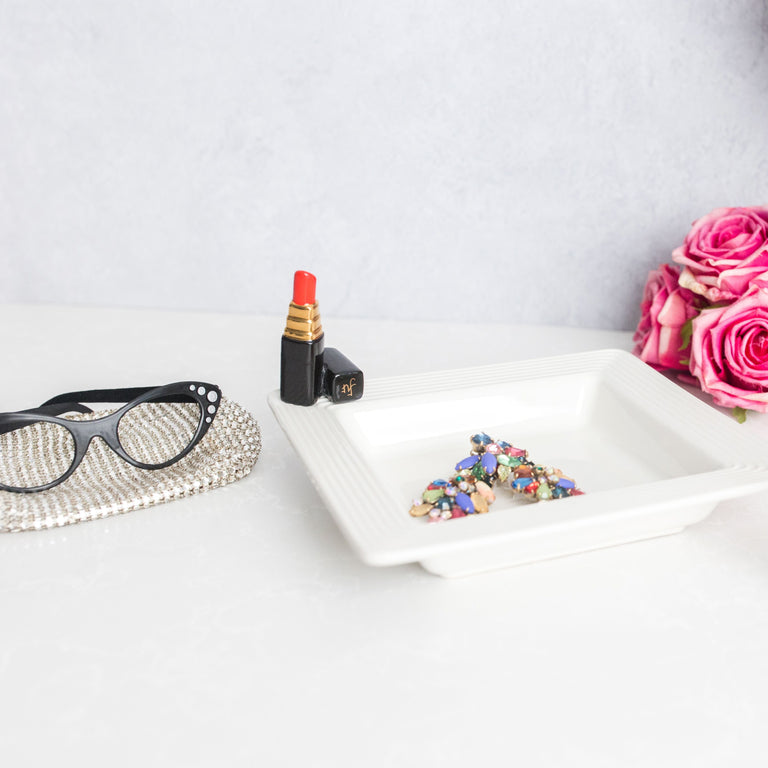 Hand-painted lipstick mini figurine attached to a white square ceramic dish with jewelry.
