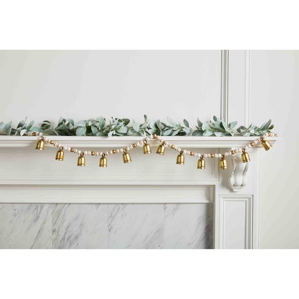 Wood bead and gold metal bell garland draped across a white fireplace mantel with green foliage.