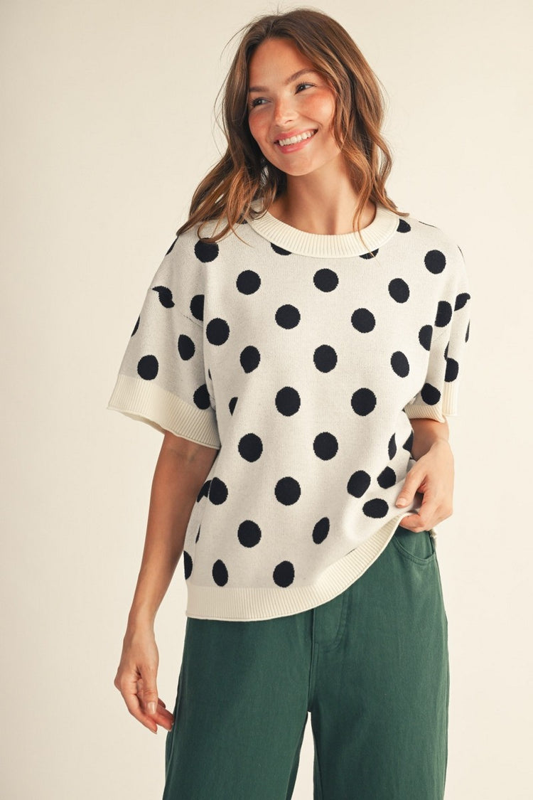Woman wearing the Emily Polka Dot Comry Sweater Top in white with black dots and green pants.