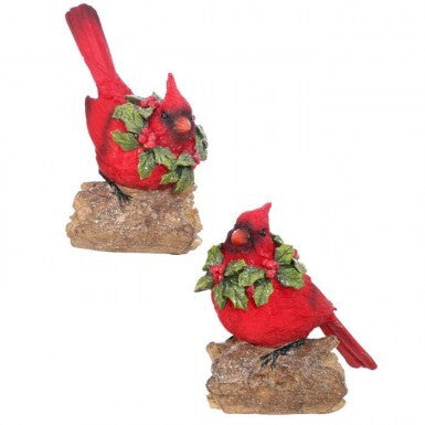 Two red resin cardinal figurines with holly wreaths perched on rustic logs.