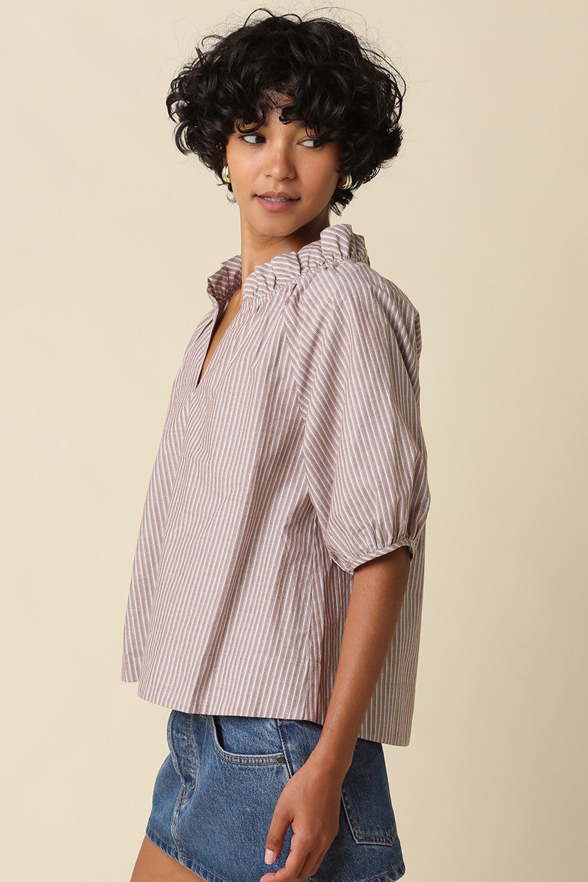 Woman wearing the Evan Stripe Puff Sleeve Blouse in a brown and white stripe with denim shorts.