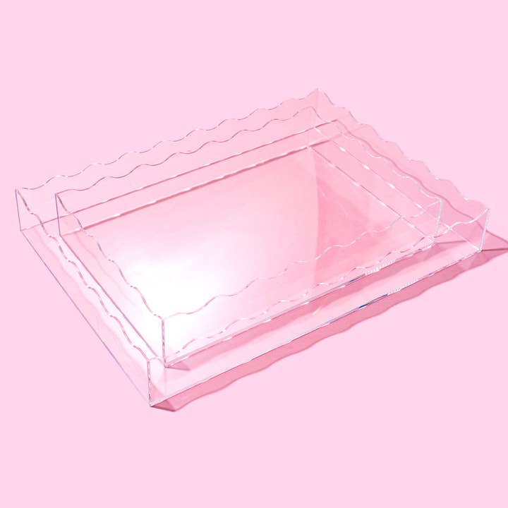 Large clear acrylic rectangular tray with wavy scalloped edges on a pink background.