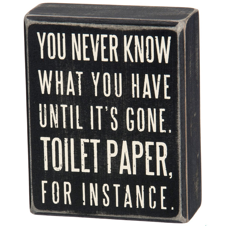 Black wooden box sign with white text reading 'You never know what you have until it's gone. Toilet paper, for instance.'