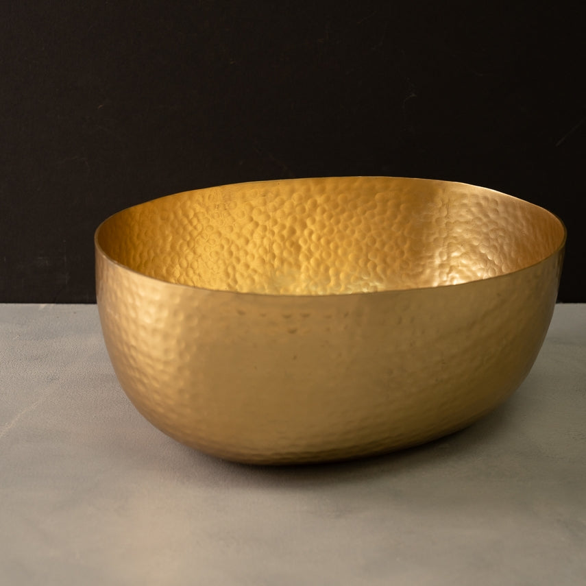 Gold aluminum hammered oval bowl with a textured finish on a grey surface.