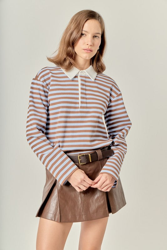 Woman wearing the Gina Rugby Polo Shirt in blue and brown stripes with a brown pleated skirt.