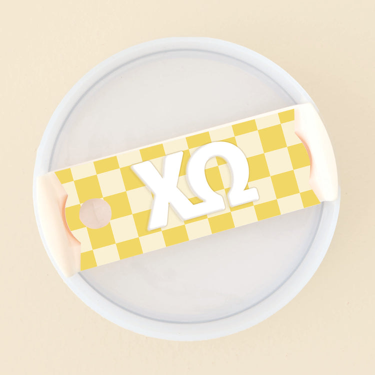 Yellow checkered acrylic tumbler lid tag with white Chi Omega Greek letters.