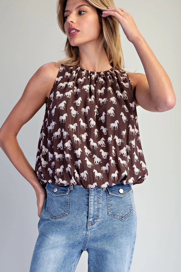 Woman wearing the Anastasia Horse Pattern Blouse in brown with white horse print and blue jeans.
