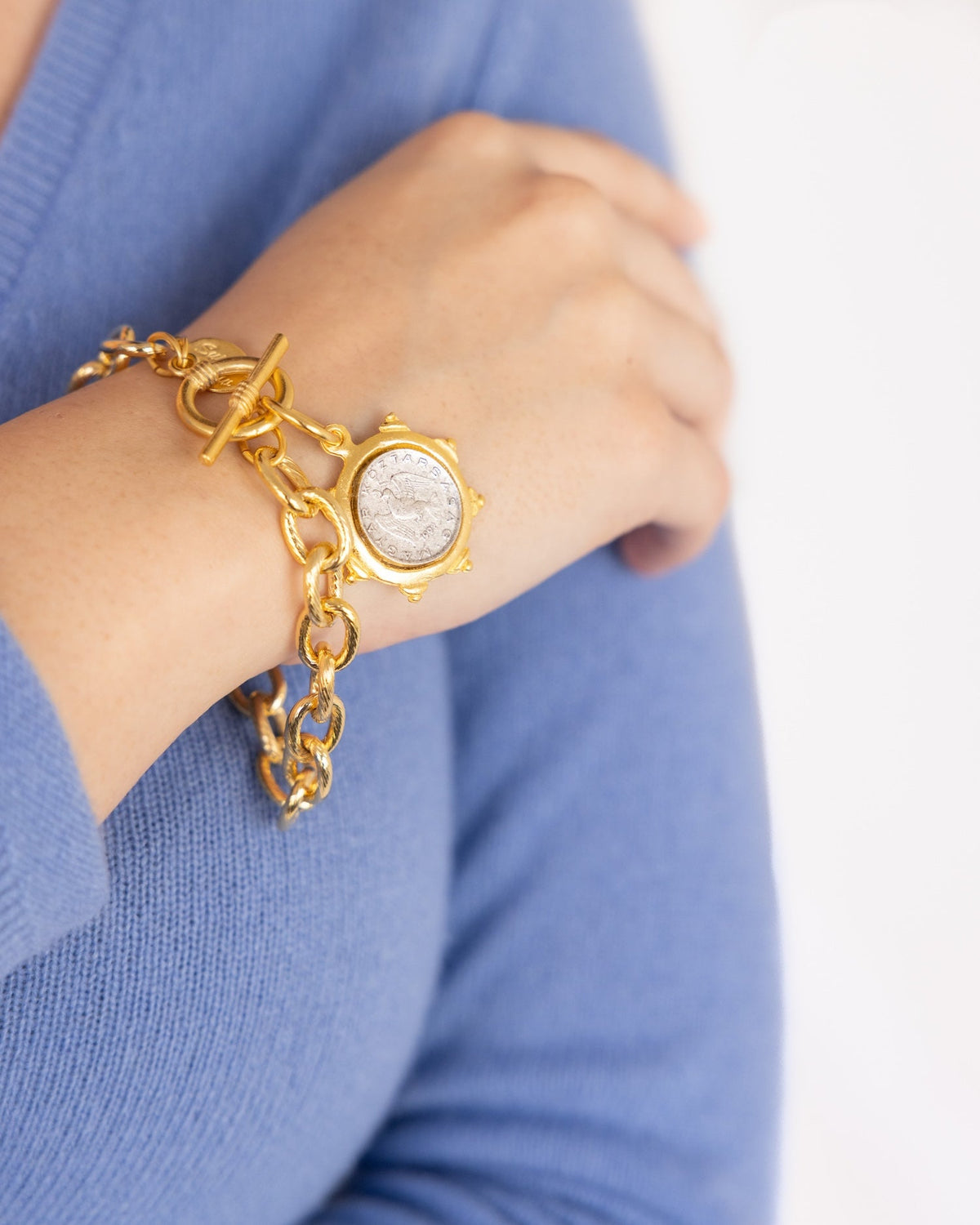 Gold chain toggle bracelet with a silver Hungarian dove coin pendant on a person's wrist.