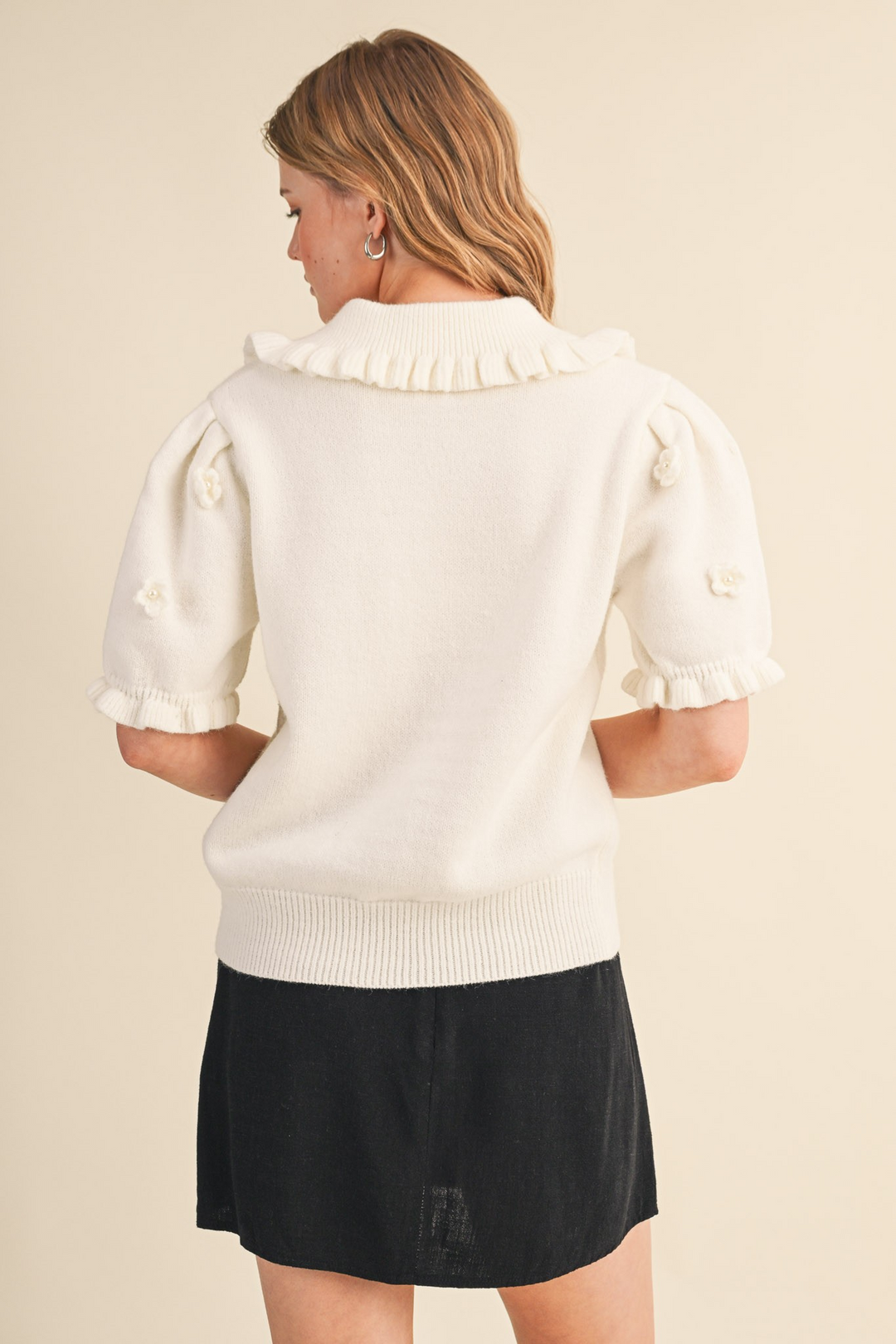 Back view of a white short-sleeved sweater with floral pearl appliqué and ruffled collar and cuffs.